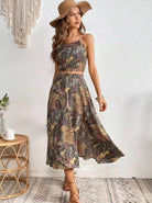 Frau im eleganten Sommerkleid mit tropischem Muster, Strohhut und Sandalen. Perfekt für Strandmode, Boho-Stil, Damenbekleidung, Sommeroutfit.