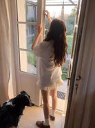 Frau öffnet Terrassentür, Border Collie schaut zu. Morgenlicht, gemütliches Zuhause, ländliche Idylle. Entspannte Atmosphäre, Naturverbundenheit.