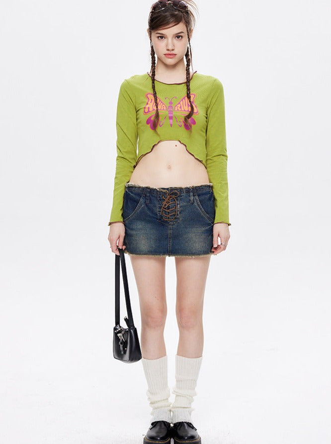 Frau in grünem Langarmshirt mit Schmetterlingsmotiv, Jeansrock, weißen Socken und schwarzen Schuhen. Modetrends, Streetwear, Damenmode.