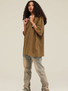 Person in lässigem Outfit: braunes Oversize-T-Shirt, helle Jeans. Modetrend, Streetwear, urbaner Stil, Freizeitlook, Unisex-Mode.