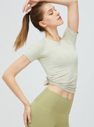 Frau in beigem Sportshirt und grüner Leggings, posiert elegant. Fitnessmode, athletische Kleidung, bequeme Sportbekleidung für Damen.