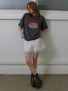Frau in grauem Oversize-T-Shirt und weißem Spitzenrock, kombiniert mit braunen Stiefeln. Modetrend, lässiger Look, Streetstyle, Damenmode.
