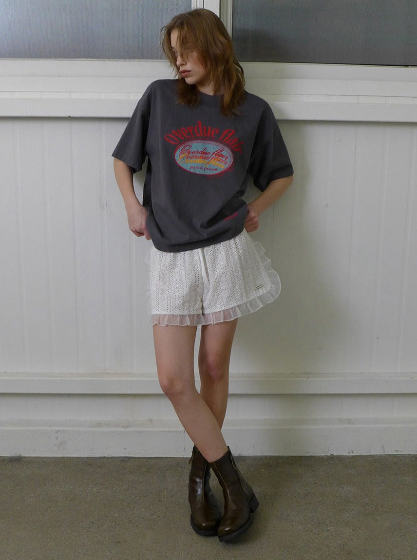 Frau in grauem Oversize-T-Shirt und weißem Spitzenrock, kombiniert mit braunen Stiefeln. Modetrend, lässiger Look, Streetstyle, Damenmode.