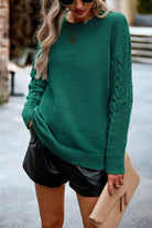 Frau in grünem Strickpullover, Leder-Shorts und Sonnenbrille, hält eine beige Clutch. Modetrend, Herbstmode, Damenbekleidung, Streetstyle.