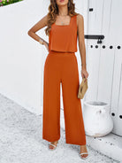 Frau in elegantem, orangefarbenem Jumpsuit vor weißer Wand, Sommermode, stilvoll, ärmellos, modisch, Damenbekleidung, trendig, Accessoires.