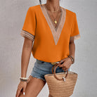 Damenmode: Orangefarbene Bluse mit V-Ausschnitt und Spitzenakzenten, kombiniert mit Jeansshorts und Strohtasche. Sommeroutfit, trendig, elegant.