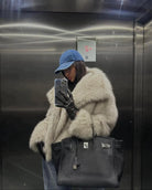 Frau im Aufzug mit Pelzmantel, blauer Kappe und schwarzer Birkin-Tasche. Mode, Luxus, Streetstyle, Winteroutfit, Accessoires.