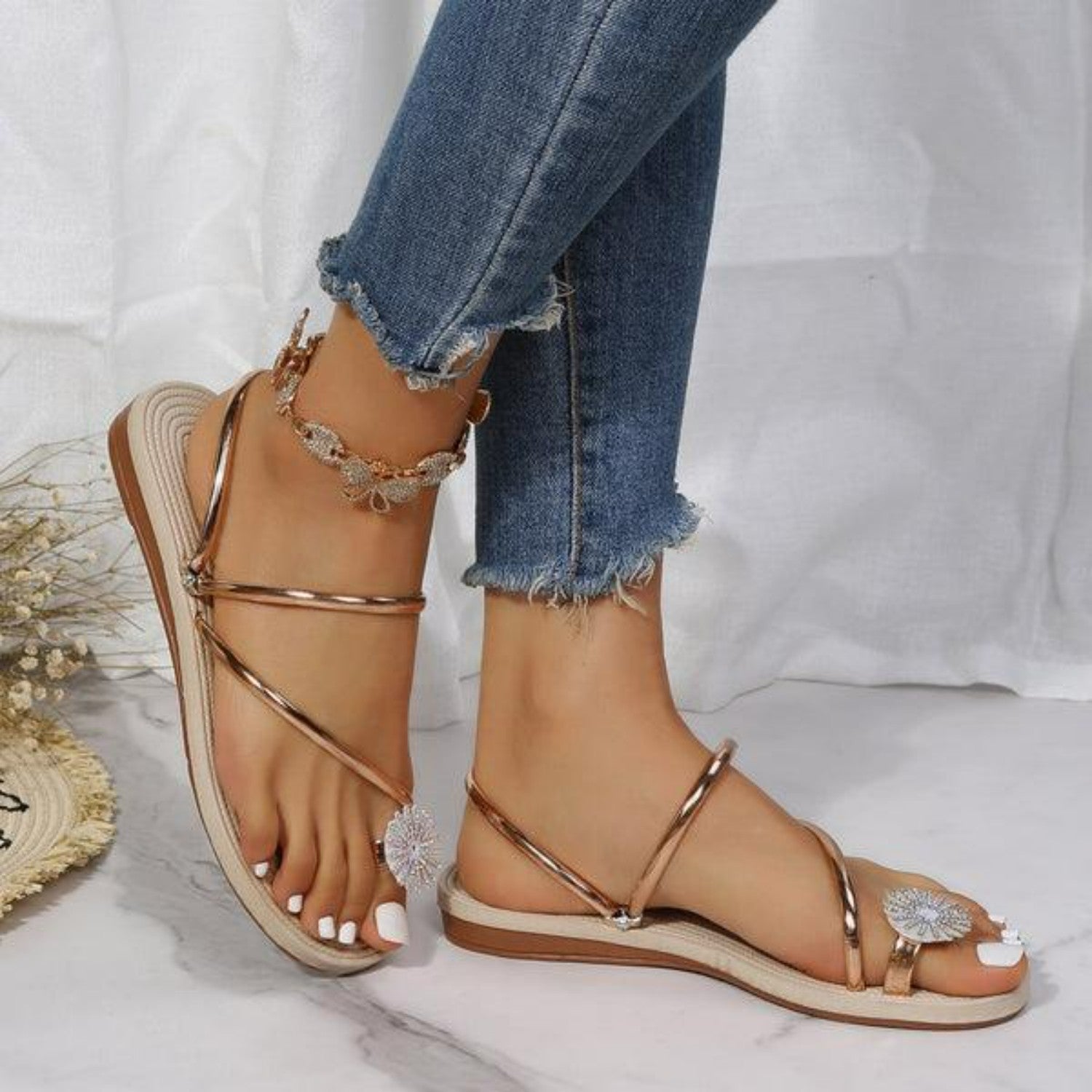 Damen Sandalen in Roségold mit Blumenapplikation, flachem Absatz und verstellbaren Riemen. Perfekt für Sommermode und Freizeitoutfits.