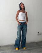 Frau in weißem Top und blauer, weiter Jeans, gelbe Schuhe, lässiger Look, Modefotografie.