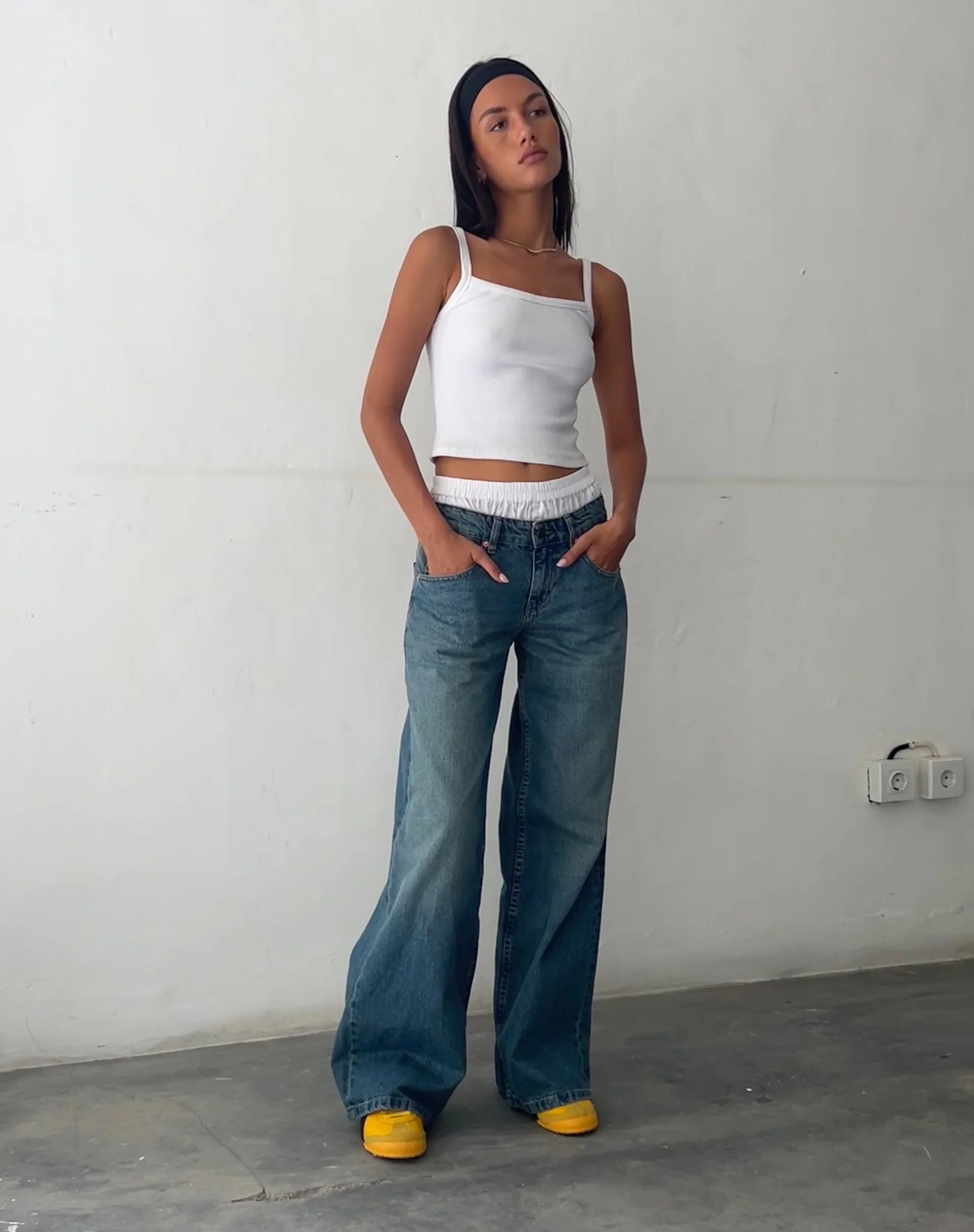 Frau in weißem Top und blauer, weiter Jeans, gelbe Schuhe, lässiger Look, Modefotografie.