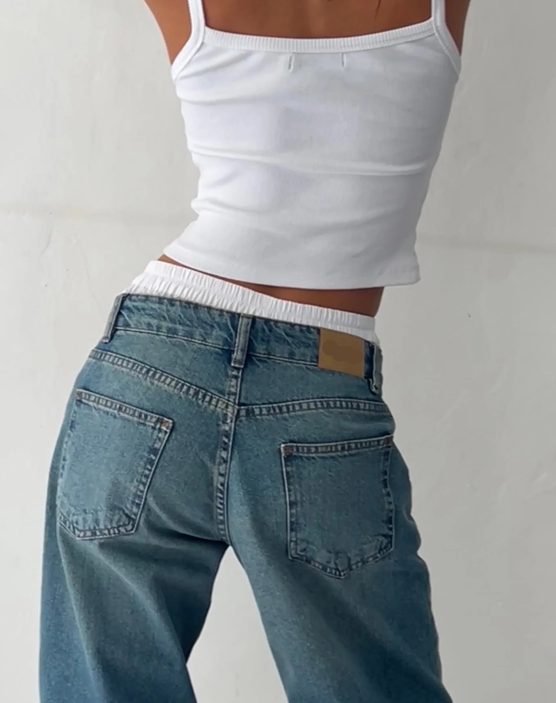 Frau in blauer Vintage-Jeans und weißem Top, modisch, lässig, Rückansicht.
