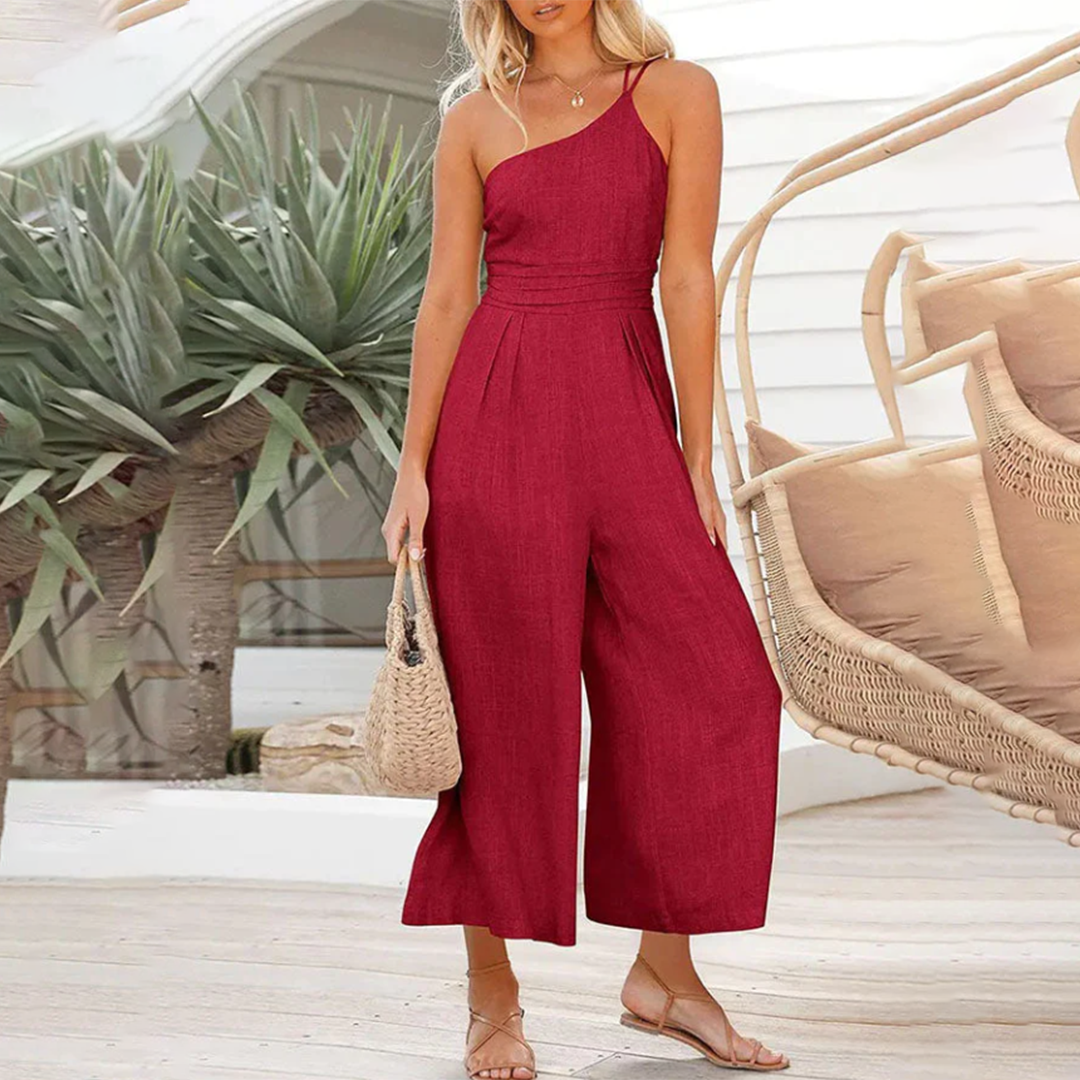 Frau in rotem Jumpsuit aus Leinen, Sommermode, mit Strohtasche, vor tropischem Hintergrund.