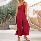 Frau in rotem Jumpsuit aus Leinen, Sommermode, mit Strohtasche, vor tropischem Hintergrund.