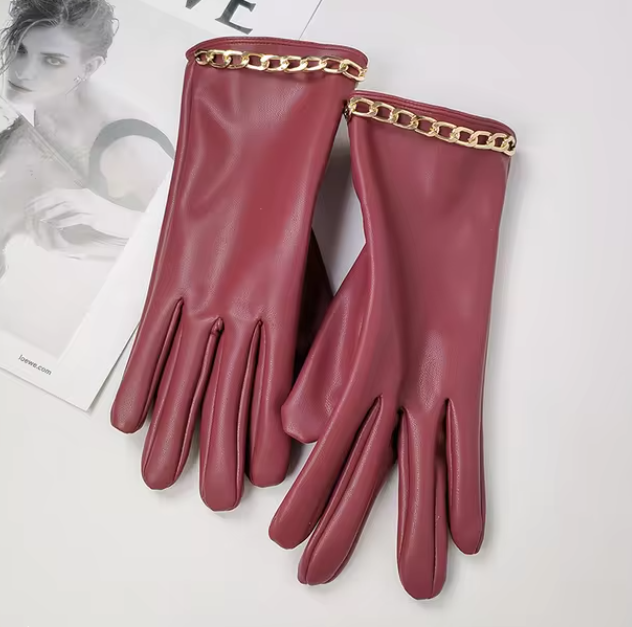 Elegante rote Lederhandschuhe mit goldener Kettenverzierung, stilvoll auf einem Magazin platziert. Perfekt für modische Herbst- und Winteroutfits.