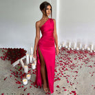 Elegantes rotes Abendkleid mit asymmetrischem Schnitt und hohem Beinschlitz, umgeben von Kerzen und Rosenblättern. Perfekt für besondere Anlässe.