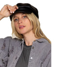 Frau mit schwarzer Lederkappe und zerrissener grauer Jacke. Modetrend, Streetwear, lässiger Look, stilvolle Accessoires, Damenmode.