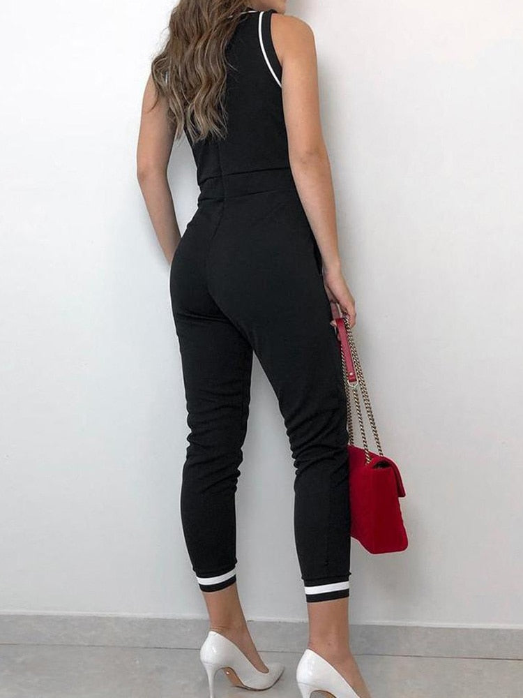 Damen Jumpsuit in Schwarz, ärmellos, mit weißen Streifen, kombiniert mit roten Handtasche und weißen High Heels. Elegante Mode für Frauen.