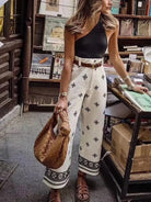 Frau in modischer Sommerkleidung: Schwarzes Top, weiße bestickte Hose, braune Sandalen. Perfekt für lässige Stadtbummel und Sommermode.
