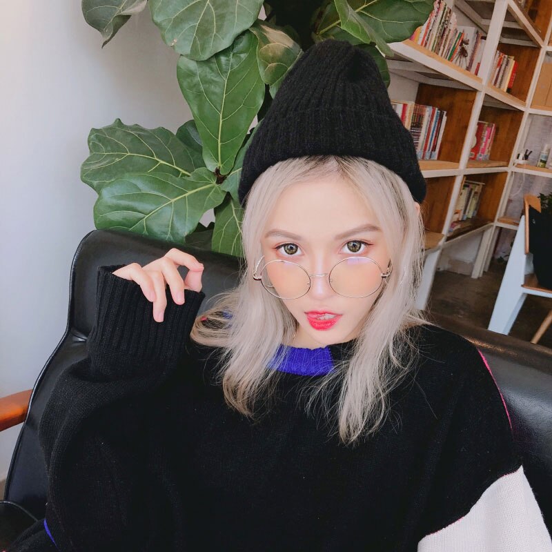 Junge Frau mit Brille und schwarzer Mütze, sitzt vor Bücherregal. Modetrend, Wintermode, stilvolle Accessoires, urbaner Look.