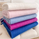 Weiche, flauschige Decken in Weiß, Rosa, Blau und Lila, gestapelt auf einem Sofa. Perfekt für gemütliche Wohnaccessoires und Heimdekoration.