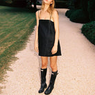 Schwarzes Minikleid, Gummistiefel, Frau im Freien, Sommermode, lässiger Stil, Gartenweg, trendiges Outfit, minimalistisches Design.