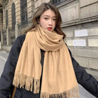 Frau mit beigem Schal und schwarzem Mantel vor städtischer Kulisse. Modetrend, Wintermode, stilvoller Look, warme Accessoires.