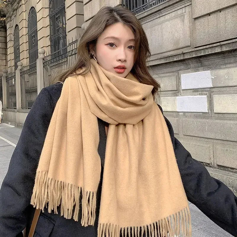 Frau mit beigem Schal und schwarzem Mantel vor städtischer Kulisse. Modetrend, Wintermode, stilvoller Look, warme Accessoires.
