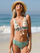 Frau im floralen Bikini und Strohhut am Strand, lächelnd in der Sonne. Sommermode, Strandbekleidung, Urlaub, Damenbademode, Strandoutfit.