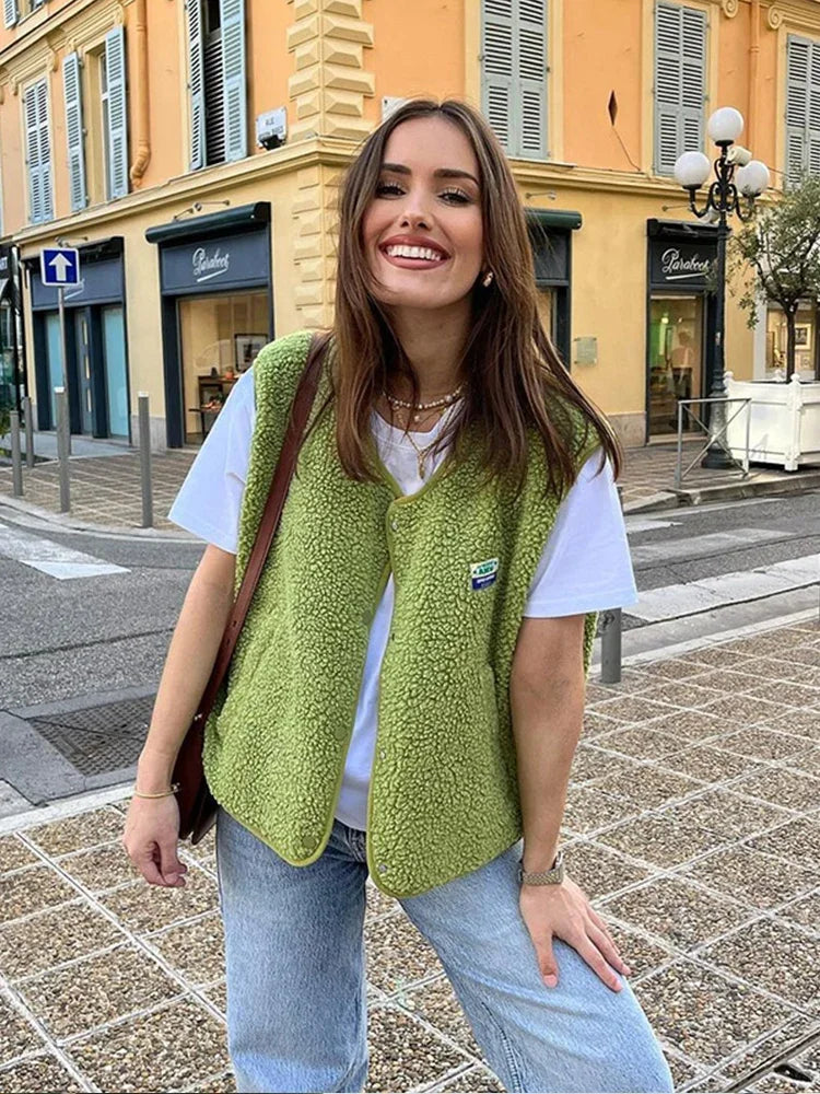 Frau in grüner Fleeceweste und weißem T-Shirt, lächelnd auf einer Stadtstraße. Modetrend, lässiger Stil, urbaner Hintergrund, Streetwear.