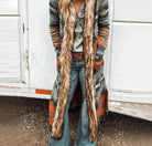 Langer Cardigan mit Ethno-Muster und Kunstfellbesatz, kombiniert mit Jeans und Gürtel. Modetrend, Boho-Stil, Damenmode, Herbstoutfit.