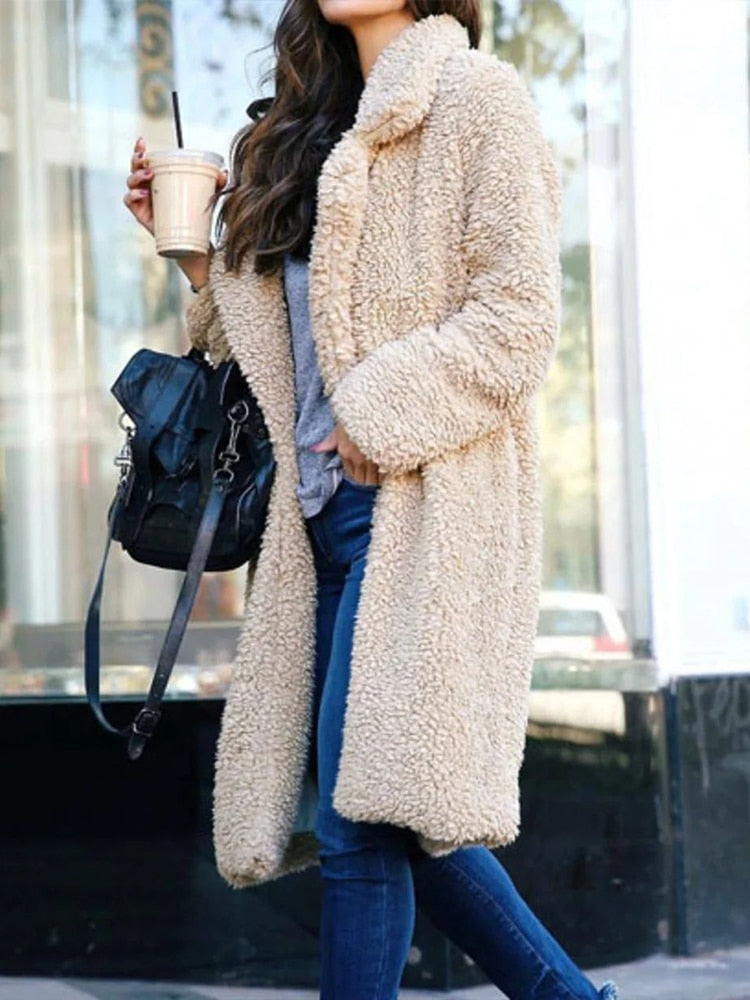 Frau in beigem Teddy-Mantel, hält Eiskaffee, trägt blaue Jeans und schwarze Tasche. Modetrend, Herbstmode, Damenbekleidung, Streetstyle.