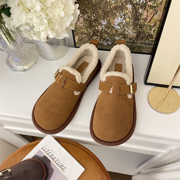 Braune Hausschuhe mit Kunstfellfutter auf weißem Tisch, neben Blumen und Buch. Bequeme, warme Pantoffeln für den Winter. Ideal für Zuhause.