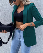 Frau in grünem Blazer, schwarzem Top und blauer Jeans, hält schwarze Handtasche. Modetrend, stilvolle Damenbekleidung, elegantes Outfit.