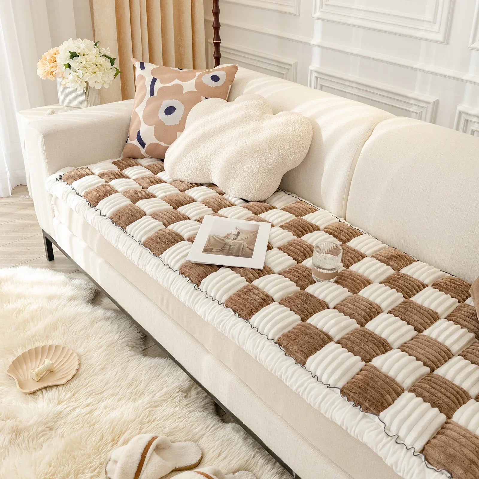 Beige Sofa mit kariertem Überwurf, dekorativen Kissen und Blumen, modernes Wohnzimmerdesign.