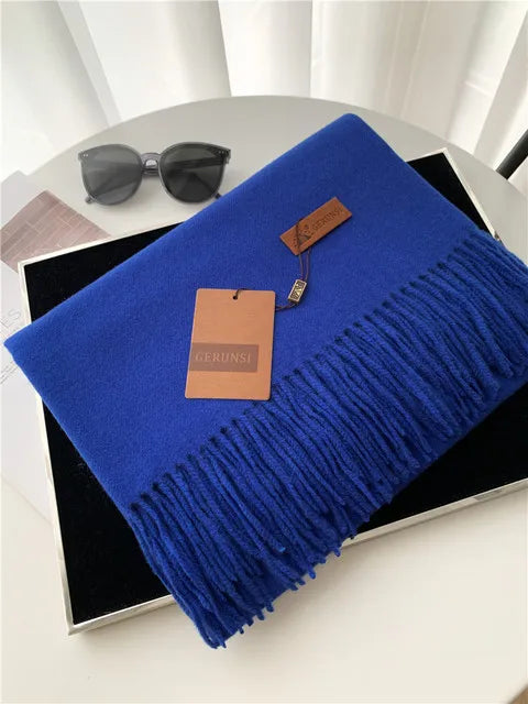 Luxuriöser blauer Schal mit Fransen aus Kaschmir, stilvoll präsentiert auf einem Tisch. Perfekt für elegante Wintermode und Accessoires.