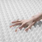 Hand drückt auf weiße Memory-Schaum-Matratze, wellenförmige Oberfläche, Komfort, Druckentlastung.