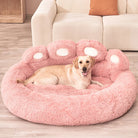 Hund auf rosa, flauschigem Hundebett in Pfotenform vor beigem Sofa im Wohnzimmer.