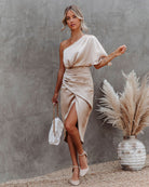 Elegantes, einseitiges Satinkleid in Beige mit asymmetrischem Schnitt, kombiniert mit weißer Handtasche und beigen High Heels. Perfekt für Abendmode.