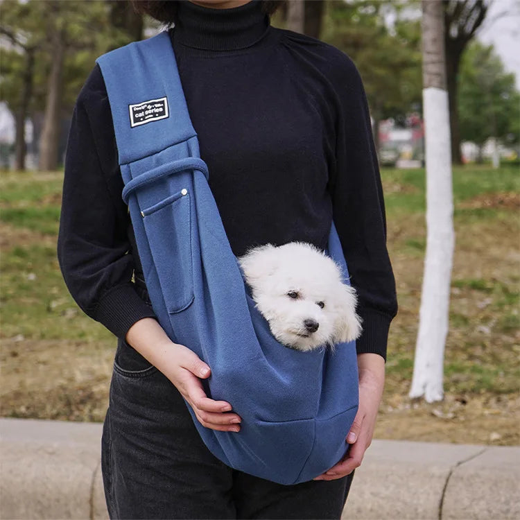 Person mit blauem Hundetragetuch, hält weißen Welpen, Outdoor, bequemes Haustierzubehör.