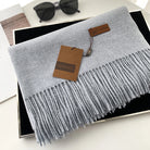 Grauer Schal mit Fransen aus Kaschmir, stilvoll präsentiert in einer Geschenkbox. Luxuriöses Accessoire, ideal für kalte Tage.