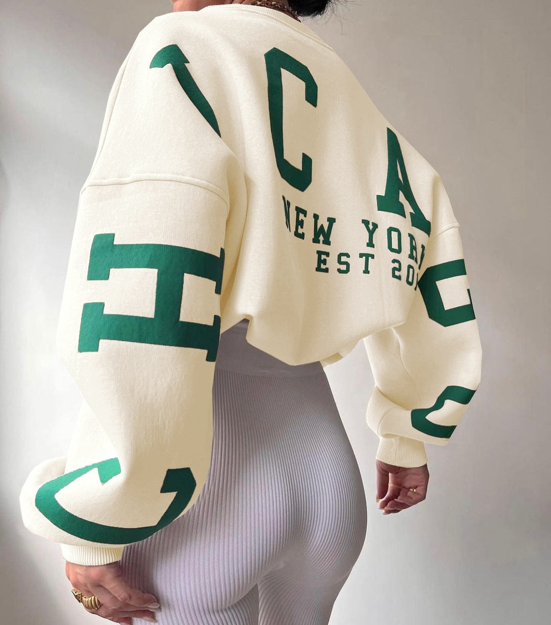 Beige Oversize-Sweatshirt mit grünen Buchstaben, New York Print, EST 2020. Modetrend, lässiger Stil, bequeme Damenbekleidung, urbaner Look.