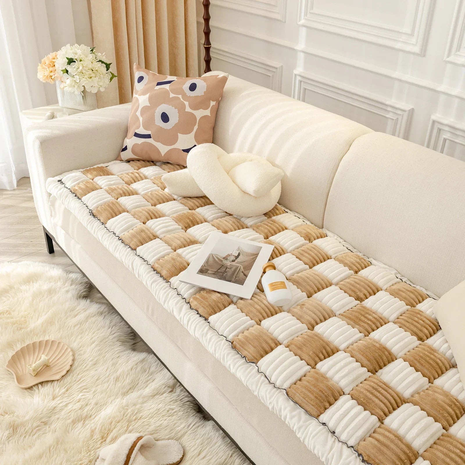 Beige-weiße Sofadecke aus Baumwolle auf cremefarbenem Sofa, dekoriert mit Kissen und Zeitschrift.