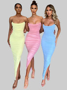 Drei Frauen in eleganten, figurbetonten Kleidern in Pastellfarben (Gelb, Rosa, Blau) mit transparenten High Heels vor grauem Hintergrund.