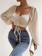 Damenmode: Elegantes, cremefarbenes Crop-Top mit Puffärmeln und Raffung, kombiniert mit modischen Jeans. Perfekt für trendige Outfits.