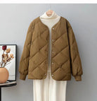 Braune, gesteppte Damenjacke auf Kleiderbügel vor grauer Wand. Modetrend, Herbstmode, warme Oberbekleidung, stilvoll, bequem.