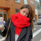 Frau mit rotem Schal und schwarzem Mantel hält Kaffeebecher, Stadtstraße im Hintergrund. Modetrend, Herbstmode, Streetstyle, Accessoires.