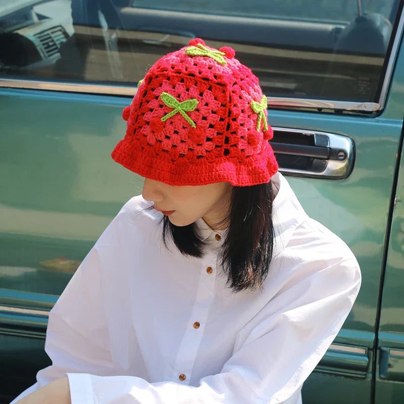 Frau mit rotem, handgestricktem Erdbeer-Hut, sitzt vor einem Auto. Modetrend, handgemachte Accessoires, auffällige Kopfbedeckung.