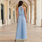 Frau in einem eleganten, blauen, plissierten Maxikleid unter Arkaden. Perfekt für Sommermode, Abendveranstaltungen, stilvolle Outfits.