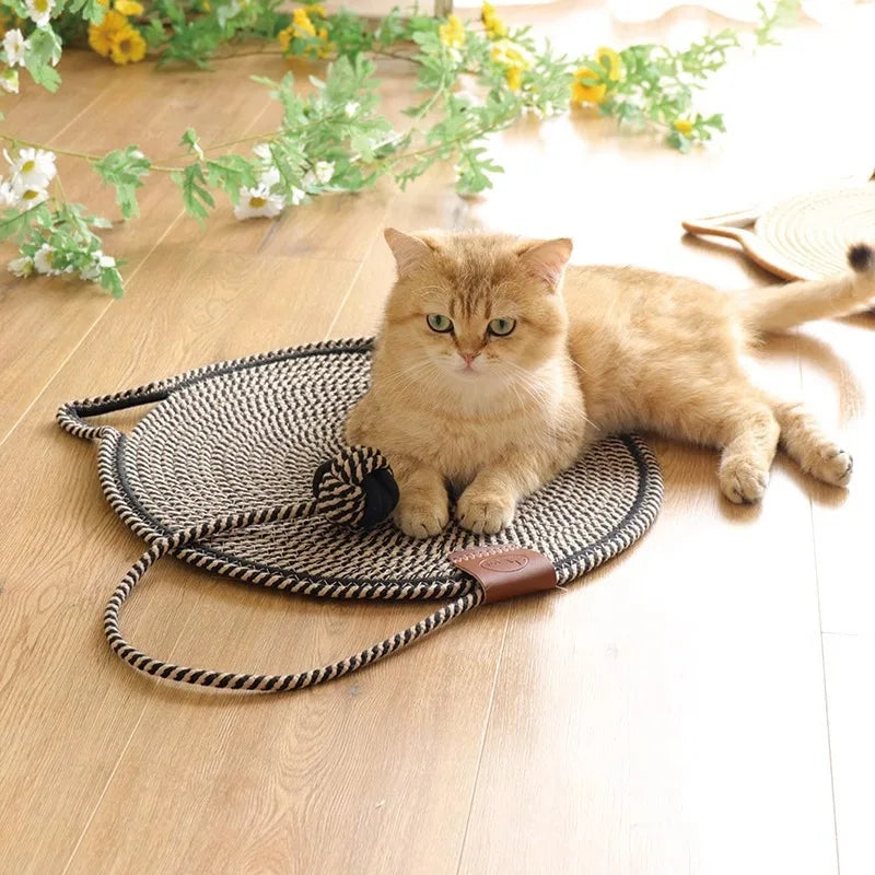 Braune Katze auf rundem, geflochtenem Katzenbett aus Seil auf Holzboden, umgeben von Blumen.