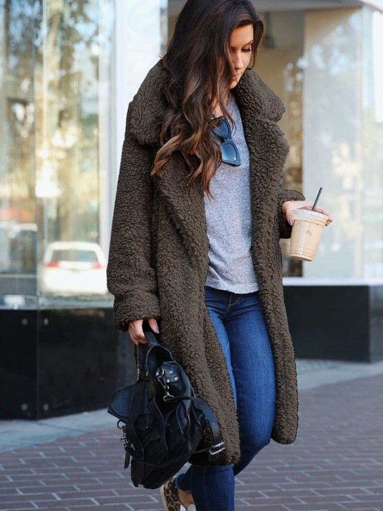 Frau in braunem Teddy-Mantel, grauem Shirt und blauer Jeans, hält Eiskaffee und schwarze Tasche. Modetrend, Herbstmode, Streetstyle.
